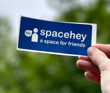 A photo of a hand holding a blue SpaceHey Sticker